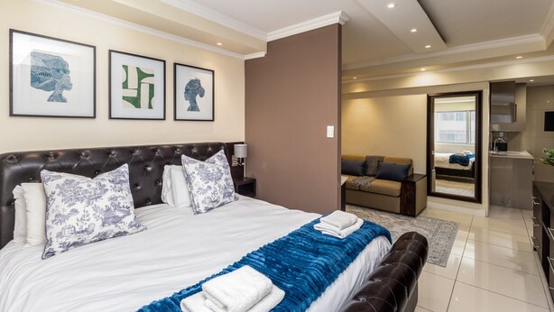 A modern hotel room with a large bed, a sofa, a desk, and a bathroom visible through an open door. - New Cumberland 405 by CTHA (Cape Town)