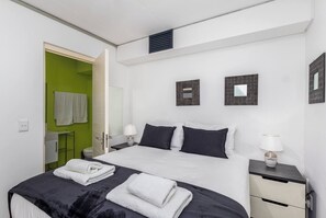 A modern hotel room with a bed, two bedside tables, a nightstand, a mirror, and a green wall. - Modern Comfort with Pool Access by Ctha (Cape Town)
