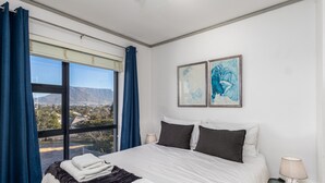 A hotel room with a large bed, two bedside tables, a window with curtains, and two framed artworks on the wall. - Key West 314 by CTHA (Cape Town)