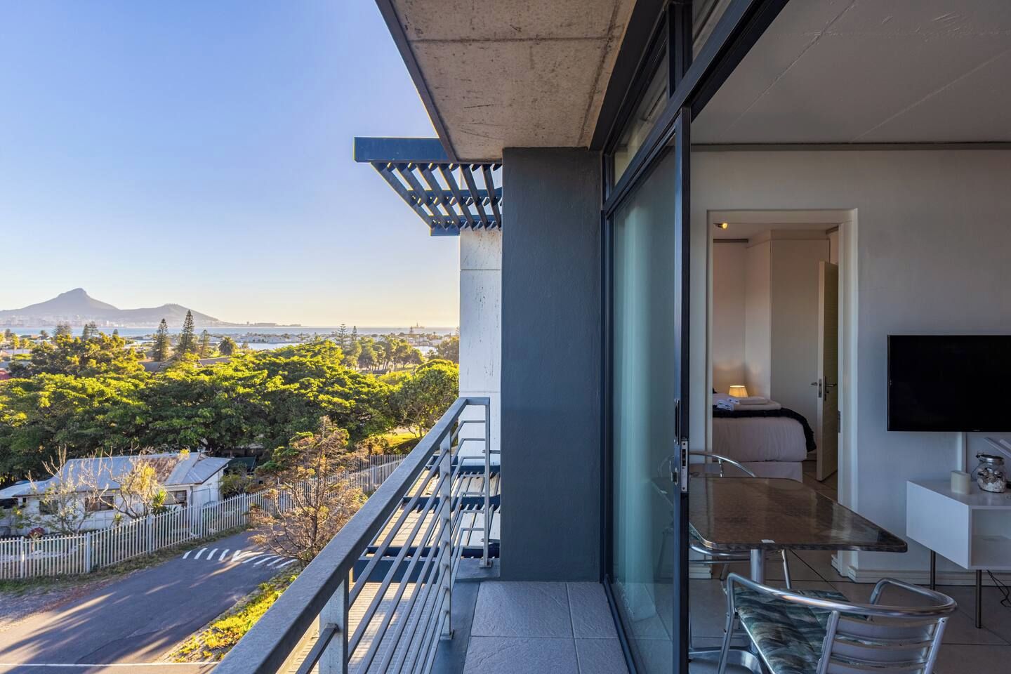 A balcony with a glass door leading to a room with a bed and a TV.