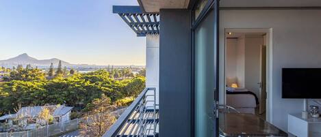 A balcony with a glass door leading to a room with a bed and a TV.