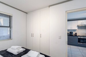 A bedroom with a bed, a wardrobe, and a view of a modern kitchen. - Modern Comfort with Pool Access by Ctha (Cape Town)