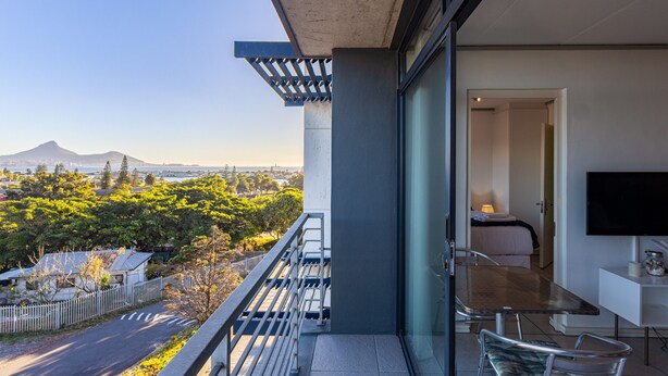 A balcony with a view of a mountain, a dining area with a table and chairs, and a TV mounted on the wall. - Key West 314 by CTHA (Cape Town)