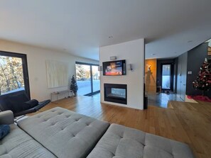 A modern living room with a fireplace, a television, and a Christmas tree.