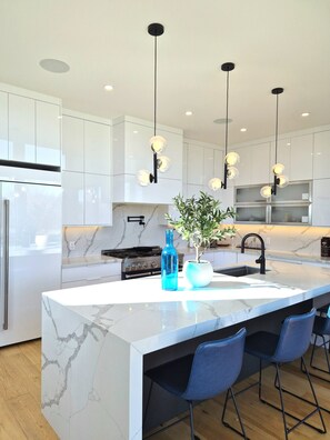 A modern kitchen with marble countertops, a central island with bar stools, stainless steel appliances, and pendant lighting. - Forest Edge Luxury  Estate (Puslinch)