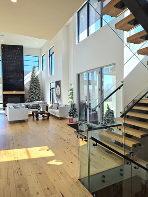 A modern living room with a staircase, wooden flooring, and a large window. - Forest Edge Luxury  Estate (Puslinch)