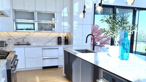 Une cuisine moderne avec des meubles blancs, un plancher en bois, un four encastré et une grande fenêtre.