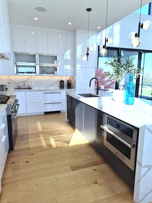 Una cocina moderna con armarios blancos, piso de madera, horno empotrado y un ventanal grande.