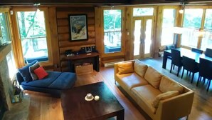 Interior de una cabaña de troncos con sofá, mesa de centro, mesa de comedor y chimenea.