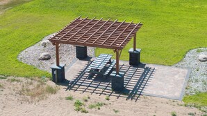 Um gazebo com cobertura de metal e bancos, cercado por uma área de cascalho e grama.