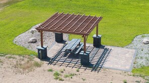 Ein Pavillon mit Metalldach und Bänken, umgeben von einer Schotterfläche und Rasen.
