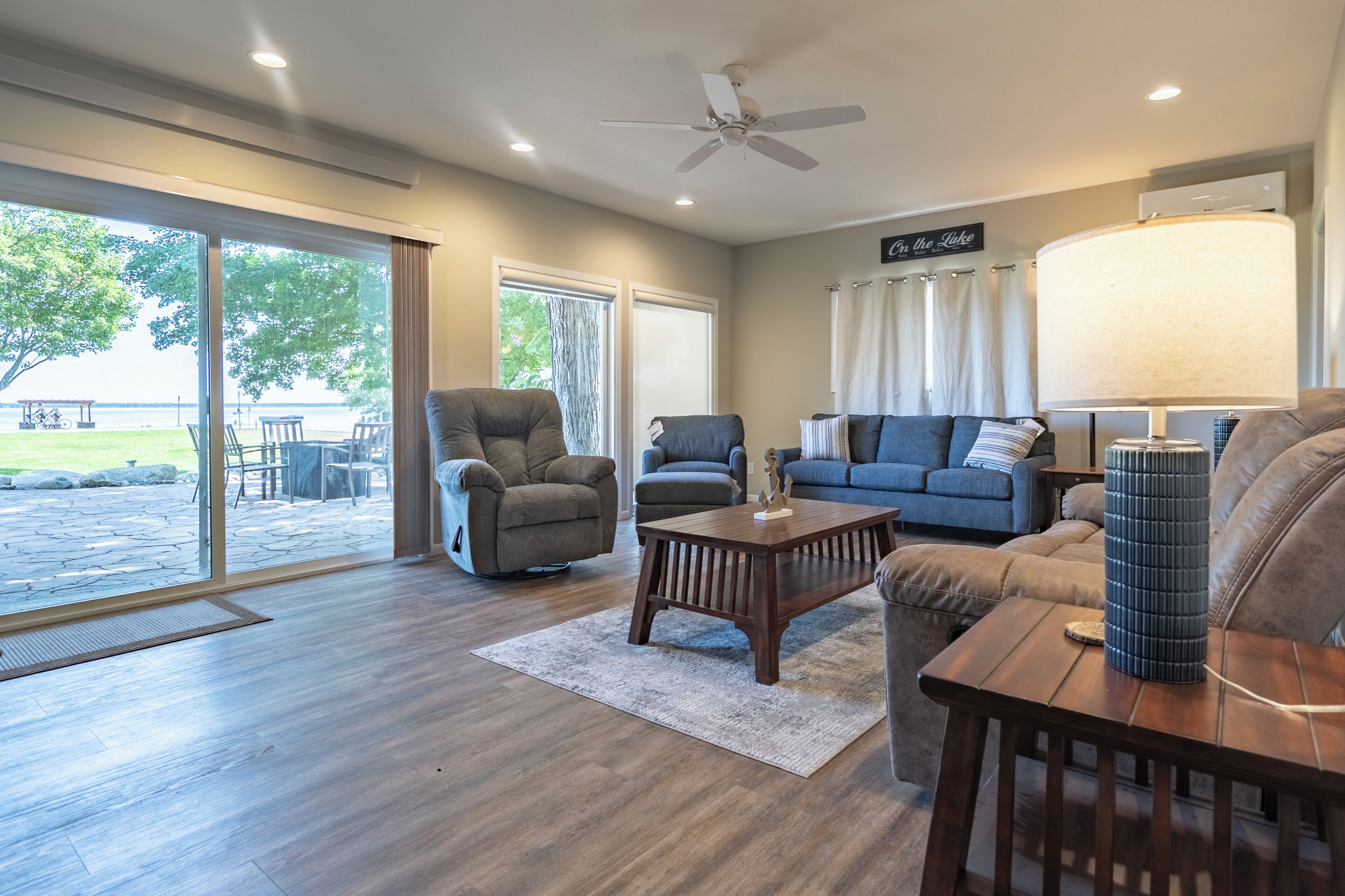 A spacious living room with a large sliding glass door leading to an outdoor area, a ceiling fan, and a sign on the wall.