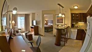 Ein Hotelzimmer mit Schreibtisch, Stuhl, Bett, Küchenzeile und Fernseher.