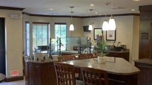 A modern kitchen with a central island, wooden chairs, pendant lighting, and a glass partition. - King Studio Suite w/ Kitchenette in Poconos (East Stroudsburg)