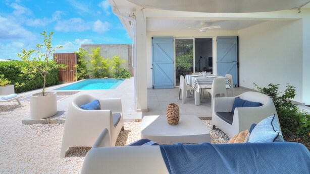 Eine Außenpatio mit weißen Möbeln, einem Pool und einem überdachten Bereich mit Tisch und Stühlen.