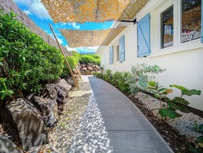 A pathway flanked by rocks and greenery, leading to a building with blue shutters. - SeaShell - New villa, private pool, tropical garden, near Le Diamant beach (LE DIAMANT)