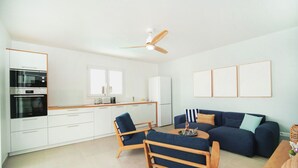 Eine moderne Küche mit integrierten Geräten, ein Essbereich mit Tisch und Stühlen, ein Sofa und ein Deckenventilator.