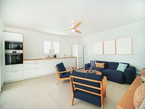 A modern kitchen with built-in appliances, a dining area with a table and chairs, a sofa, and a ceiling fan. - SeaShell - New villa, private pool, tropical garden, near Le Diamant beach (LE DIAMANT)