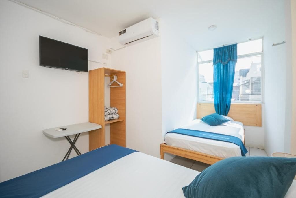 A bedroom with a bed, a TV, a wardrobe, a small table, and a window with curtains.