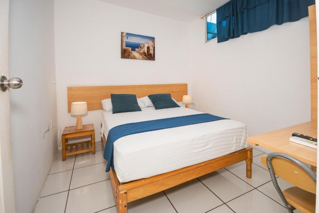 A bedroom with a wooden bed, two bedside tables with lamps, a desk, and a chair.