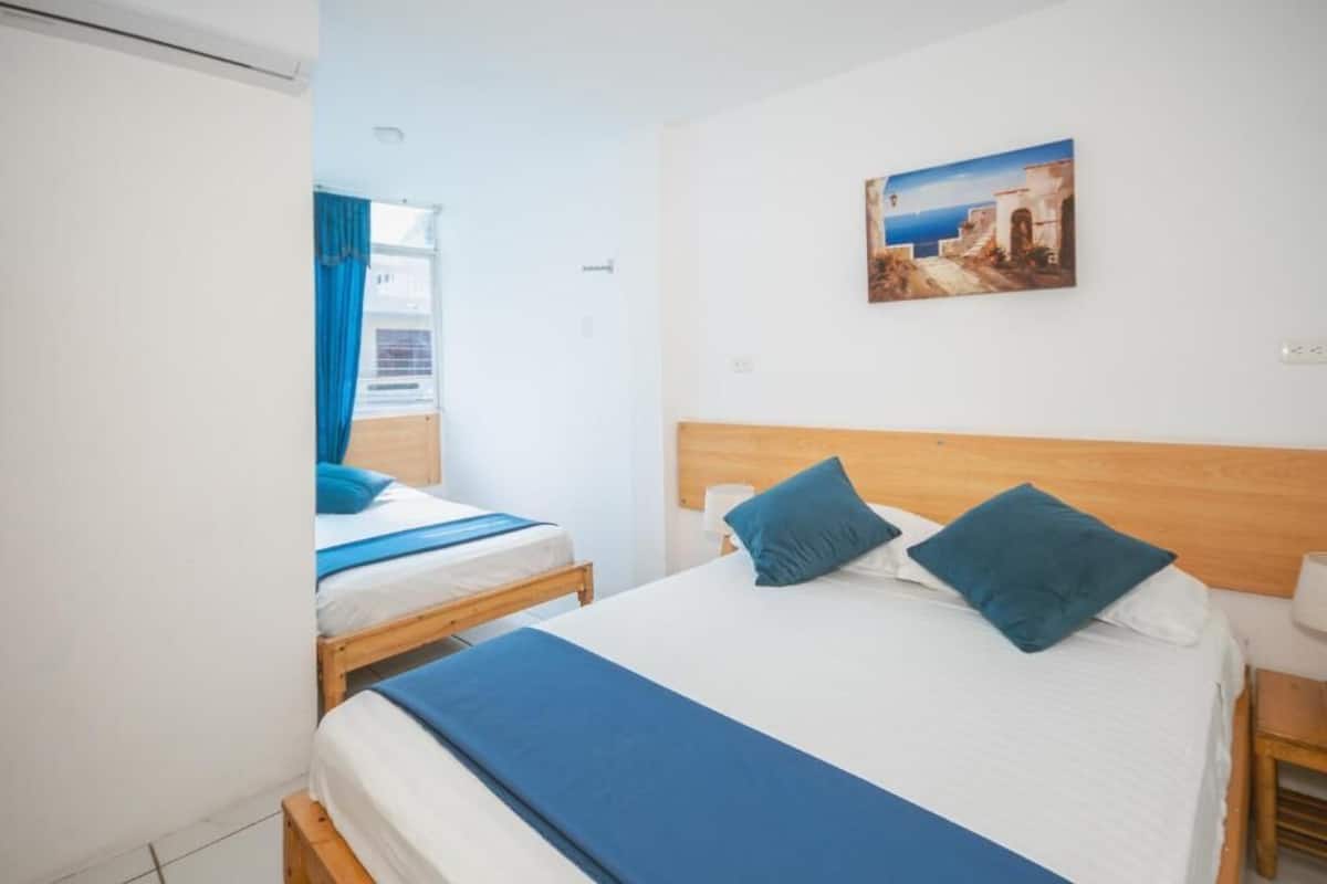 A hotel room with two beds, a wooden headboard, a painting on the wall, and a window with curtains.