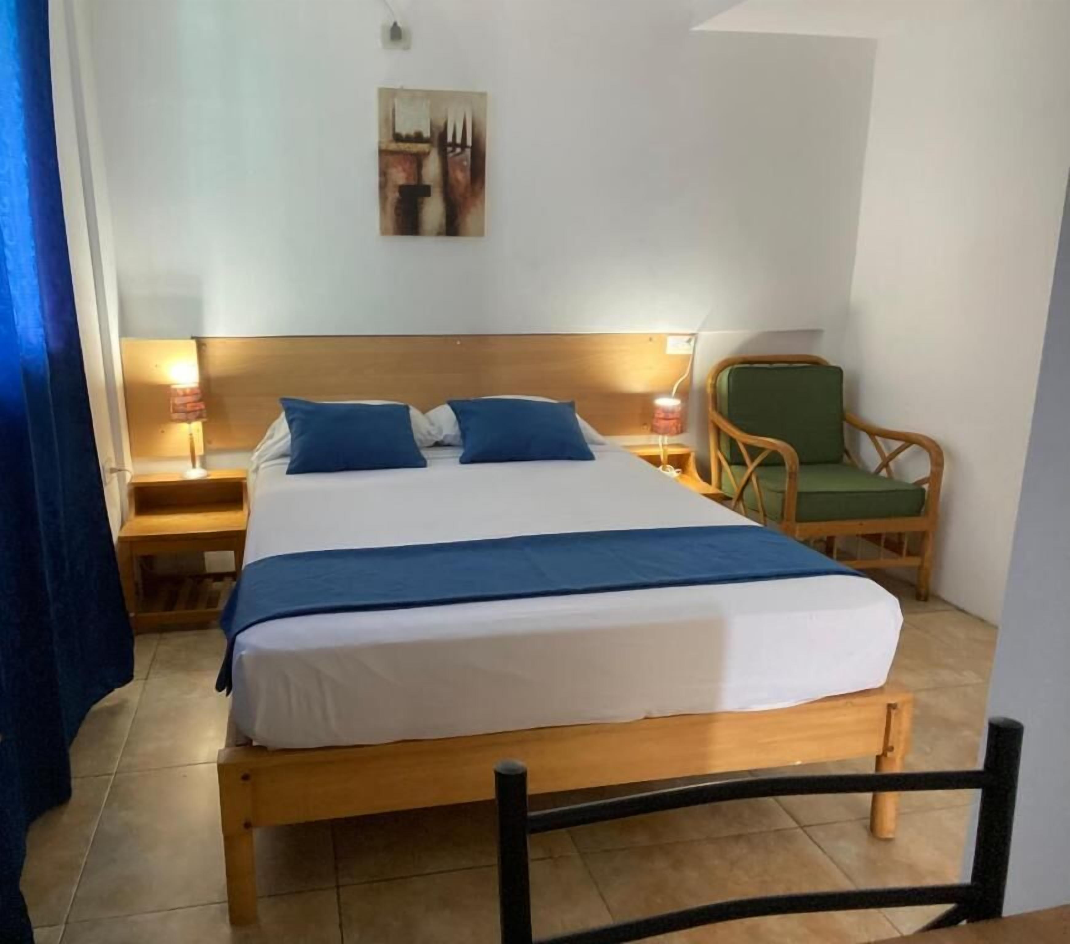 A bed with a wooden frame, two bedside tables, a green chair, and a wall-mounted picture.