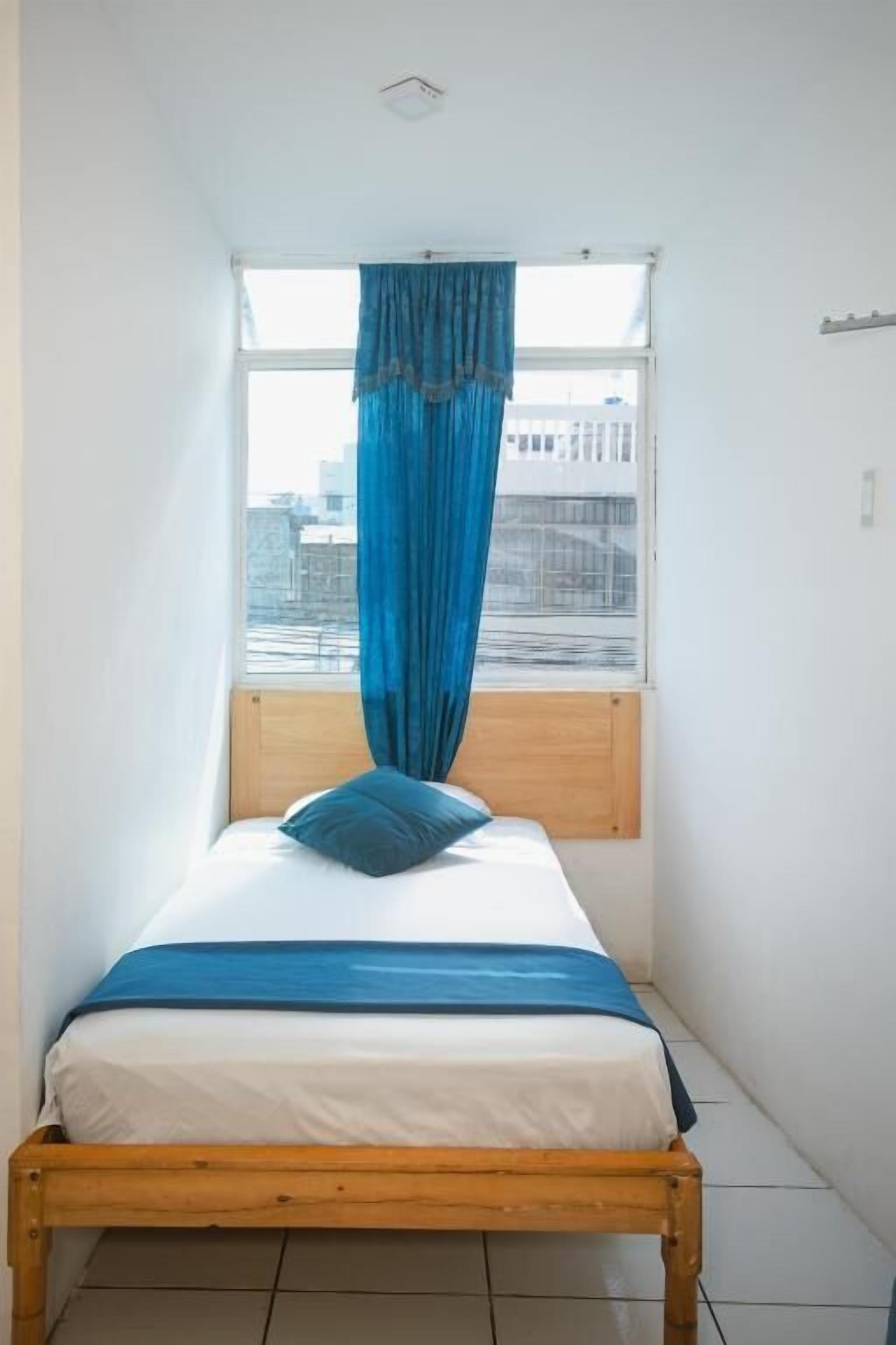 A single bed with a wooden frame, a white mattress, and a blue bedspread.