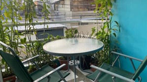 A small round table with a metal frame, surrounded by green chairs, set on a balcony with potted plants and a view of buildings. - HOTEL CASA LATINA MANTA (Manta)