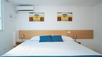 Habitación de hotel con una cama, dos cuadros en la pared, cabecera de madera, mesitas de noche con lámparas y un equipo de aire acondicionado.