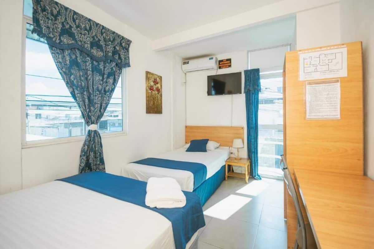 A hotel room with two beds, a television, an air conditioning unit, and a wooden desk.