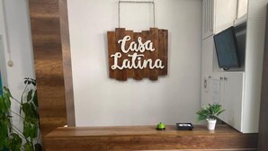 A reception desk with a wooden finish, a sign that reads 'Tasa Latina', and a potted plant on the counter. - HOTEL CASA LATINA MANTA (Manta)