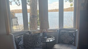 A cozy seating area with two armchairs and a small table, a large window with a view of a lake, and a framed quote on the wall.