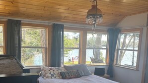 A bedroom with a large bed, a wooden ceiling, and a view of a lake.