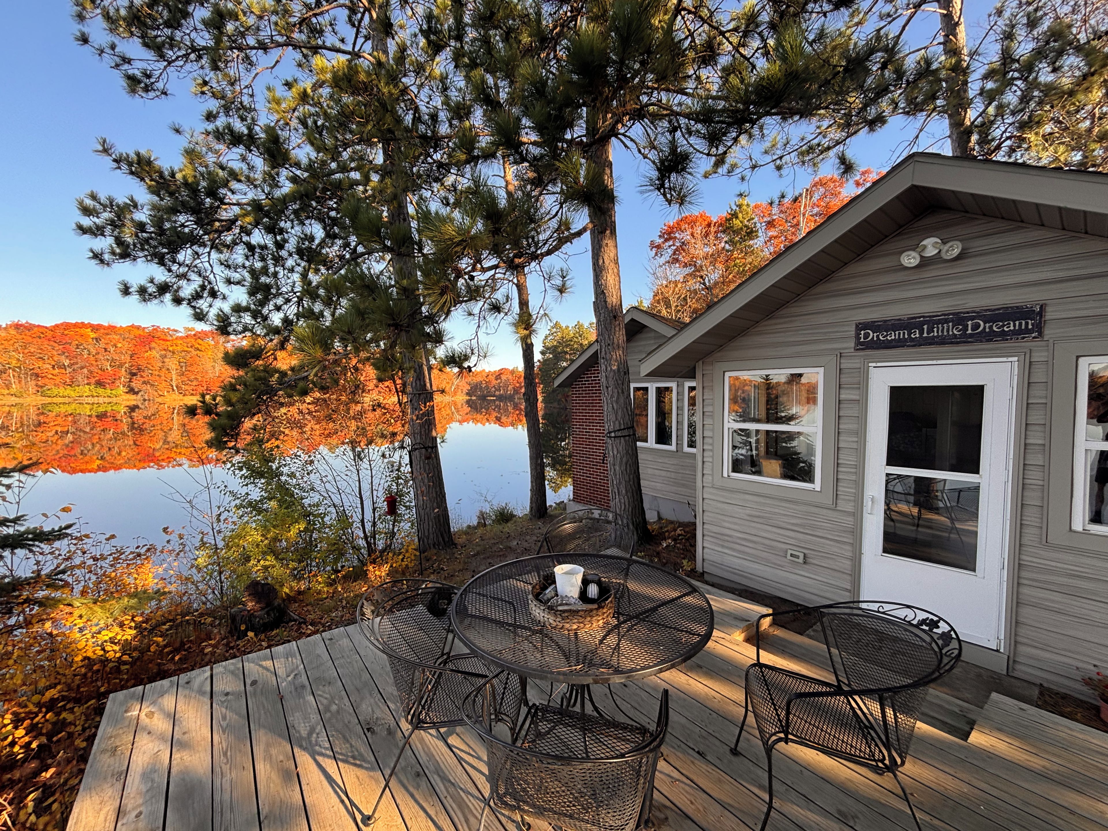 Una cabaña con terraza, mobiliario exterior y vistas a un lago y el follaje otoñal.