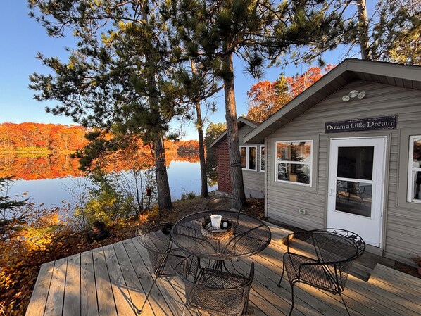Una cabaña con terraza, mobiliario exterior y vistas a un lago y el follaje otoñal.