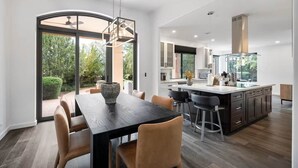 A modern kitchen with a large island, dark wood flooring, and a dining area with a large table and chairs. - Chapel Showstopper! Walk to trails, Private yard (Sedona)