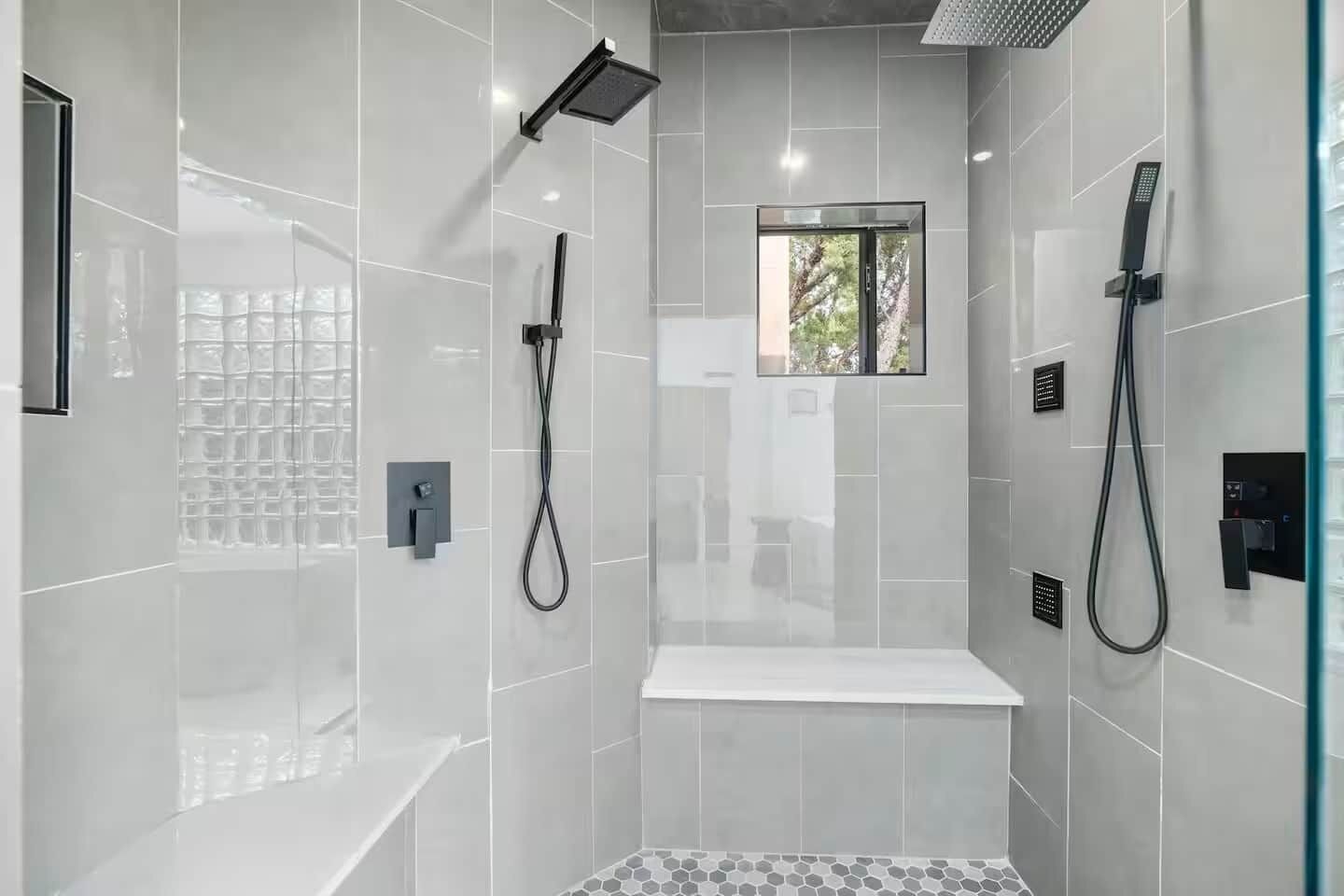 A modern shower area with a glass enclosure, a bench, and a window.