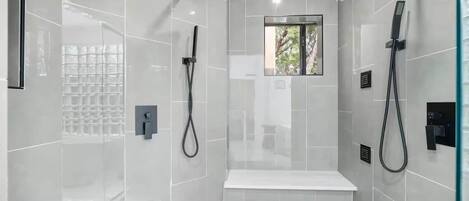 A modern shower area with a glass enclosure, a bench, and a window.