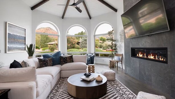A living room with a white sofa, a round coffee table, a fireplace, and large windows. - Chapel Showstopper! Walk to trails, Private yard (Sedona)