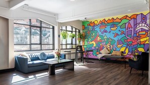 A modern living room with a colorful mural, a blue sofa, a coffee table, and a black armchair. - HI Vancouver Downtown - Hostel (Vancouver)