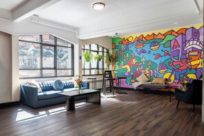 A modern living room with a colorful mural, a blue sofa, a coffee table, and a black armchair.