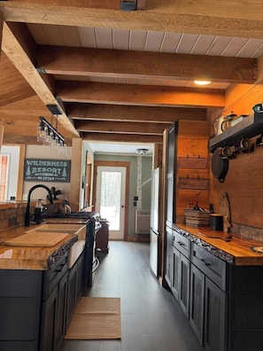 A rustic kitchen with wooden beams, a central island, and a sign reading 'WILDERNESS RESORT ROUGHING IT IN STYLE.' - Charming 2-bedroom house in Rockwood perfect for unplugging! (Rockwood)