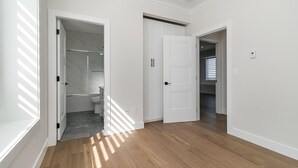 A hallway with wooden flooring, white walls, and a bathroom with a toilet and shower visible. - 🏡 Upscale COZY 2BR Coastal Suite  Private Entry, Laundry & Minutes to the Beach (Surrey)