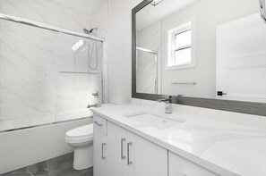 Un baño moderno con ducha envuelta en cristal, inodoro blanco y un espejo grande sobre un lavabo blanco.