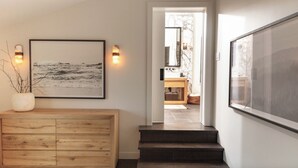 A hallway with a wooden cabinet, a framed picture, and a staircase leading to a bathroom with a marble wall and a mirror. - West Vancouver Ambelside Mid-Century Home (West Vancouver)