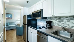 Una cocina moderna con armarios blancos, microondas integrado, cafetera y pileta de acero inoxidable.