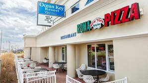 Un restaurante llamado 'ROMA New York Style Pizza' con mesas al aire libre y un letrero que indica 'Ocean Key Resort' al fondo.