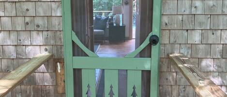 A wooden door with a green frame and a cut-out design of trees, leading to an interior space with a sofa and a lamp.