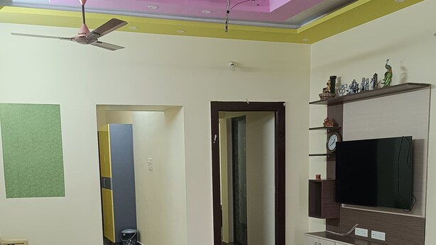 A spacious living area with a flat-screen TV, a ceiling fan, and a marble floor.