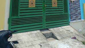 A two-story building with a green gate, a balcony, and a window with a metal grill.